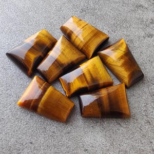 Può includere: Sette cabochon di occhio di tigre lucidati in varie dimensioni e forme, con un colore marrone dorato e un effetto scintillante.