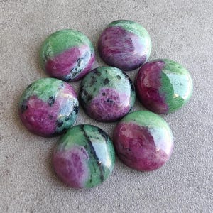 以下が含まれることがあります： 緑とピンクの宝石のカボションが7つ。カボションは滑らかで磨かれた表面を持ち、円形に配置されています。