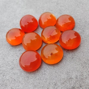 May include: A group of nine smooth, round, orange carnelian stones. The stones are polished and have a glossy finish.