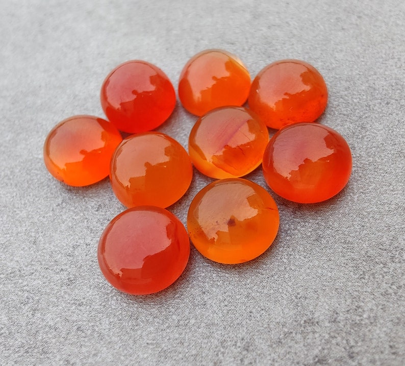 May include: A group of nine smooth, round, orange carnelian stones. The stones are polished and have a glossy finish.