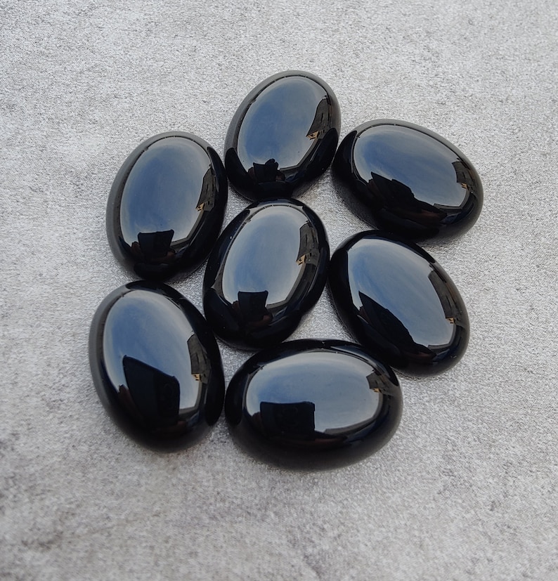 May include: Seven smooth, black oval-shaped gemstones. The stones are polished and have a glossy finish.
