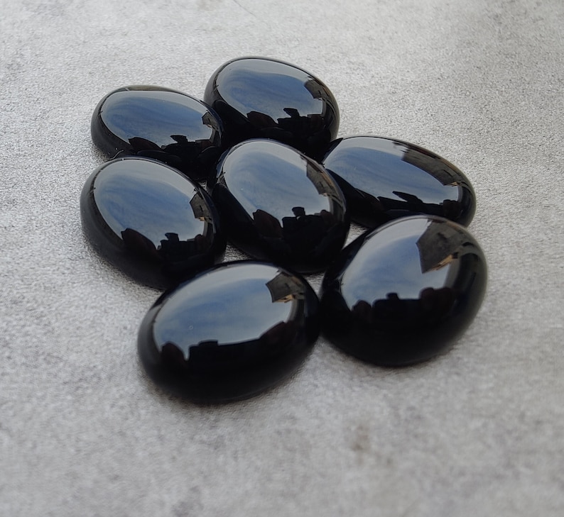 May include: Seven smooth, oval-shaped black gemstones. The stones are polished and have a glossy finish.