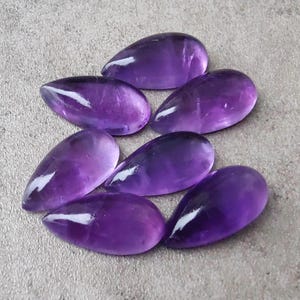Op de afbeelding: Zeven paarse amethist edelstenen cabochons in een traanvorm.