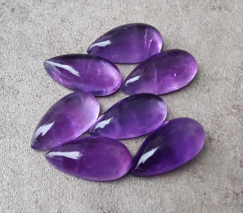 Op de afbeelding: Zeven paarse amethist edelstenen cabochons in een traanvorm.