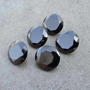 Puede incluir: Cinco gemas negras redondas y facetadas dispuestas sobre una superficie gris. Las gemas tienen un acabado brillante y reflejan la luz, mostrando su corte. Las gemas son probablemente para la fabricación de joyas o coleccionar.