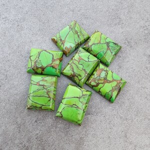 Puede incluir: Siete cabujones de turquesa verde y dorada, cortados en forma rectangular, están dispuestos sobre una superficie gris.