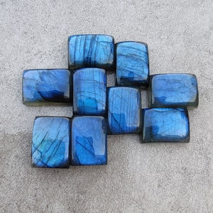 May include: A collection of ten blue labradorite gemstone cabochons, cut and polished into rectangular shapes. The stones have a shimmering, iridescent quality.