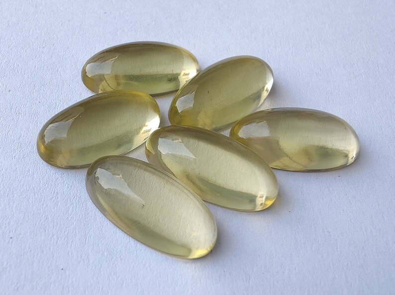 May include: Six oval-shaped, translucent yellow gemstones. The gemstones are smooth and polished, with a slight sheen.