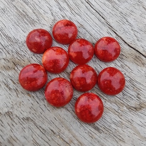 Peut inclure: Dix cabochons ronds en corail rouge. Les cabochons sont lisses et polis, avec une surface légèrement texturée.