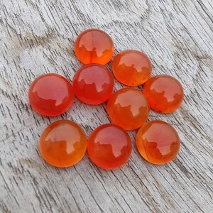 May include: Eight round, orange carnelian cabochons, polished and smooth, arranged in a loose cluster on a light wood surface.