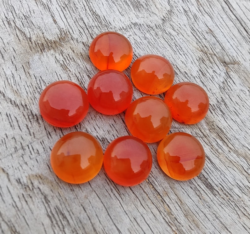 May include: Eight round, orange carnelian cabochons, polished and smooth, arranged in a loose cluster on a light wood surface.