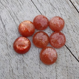 May include: Seven round, orange sunstone cabochons with a sparkly, iridescent finish. The stones are approximately 1 inch in diameter.