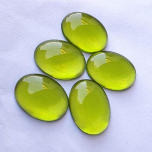 May include: Five oval-shaped, bright green gemstones. The gemstones are smooth and polished, with a glossy finish.