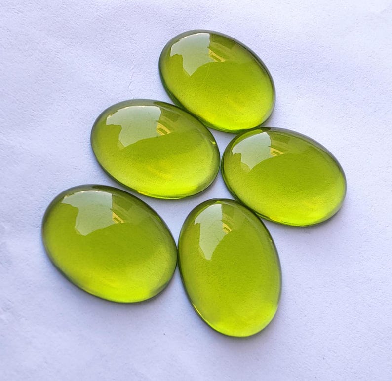 May include: Five oval-shaped, bright green gemstones. The gemstones are smooth and polished, with a glossy finish.