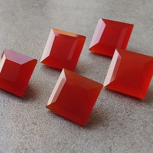 May include: Five red carnelian gemstone cabochons cut into square shapes. The stones are polished and have a smooth, glossy finish.