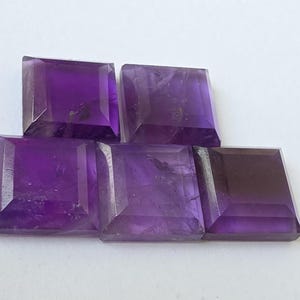 Peut inclure: Cinq pierres pr&eacute;cieuses d'am&eacute;thyste taill&eacute;es en carr&eacute;, de diff&eacute;rentes nuances de violet. Les pierres sont dispos&eacute;es en quinconce, mettant en valeur leurs surfaces &agrave; facettes et leur couleur riche. Les pierres sont probablement destin&eacute;es &agrave; la joaillerie.