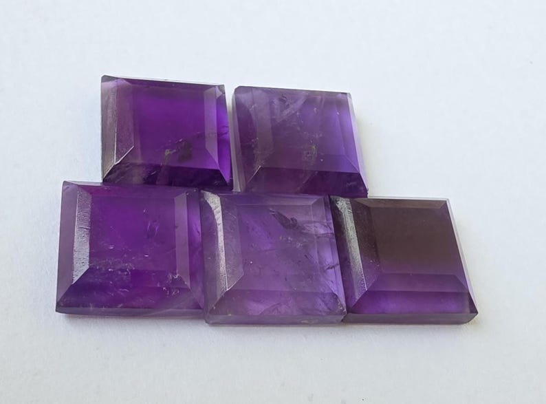 Peut inclure: Cinq pierres pr&eacute;cieuses d'am&eacute;thyste taill&eacute;es en carr&eacute;, de diff&eacute;rentes nuances de violet. Les pierres sont dispos&eacute;es en quinconce, mettant en valeur leurs surfaces &agrave; facettes et leur couleur riche. Les pierres sont probablement destin&eacute;es &agrave; la joaillerie.