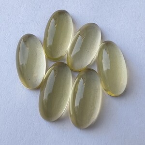 May include: Six oval-shaped, translucent, light yellow gemstones. The gemstones are smooth and polished.