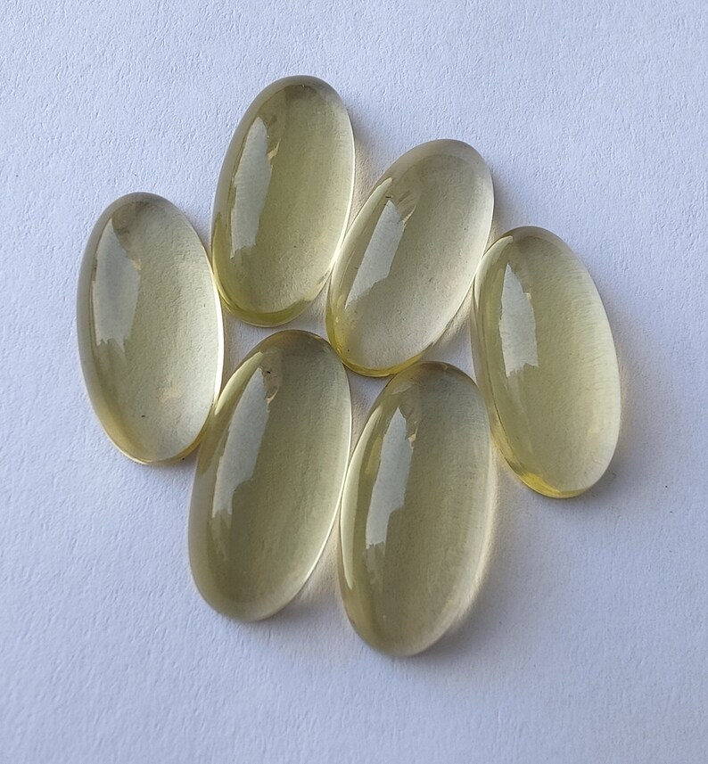 May include: Six oval-shaped, translucent, light yellow gemstones. The gemstones are smooth and polished.