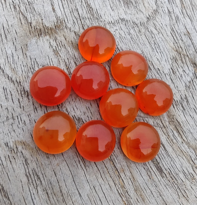 May include: Nine round, orange carnelian cabochons, polished and smooth, arranged in a triangular pattern on a wooden surface.