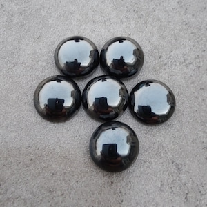 May include: Six black, round, shiny glass cabochons. The cabochons are arranged in a circle with one in the center.