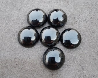 May include: Six black, round, shiny glass cabochons. The cabochons are arranged in a circle with one in the center.