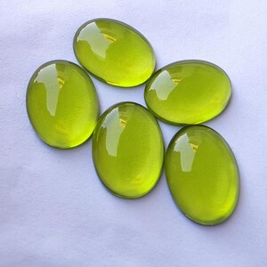 May include: Five oval-shaped, translucent green glass cabochons. The cabochons are smooth and shiny.