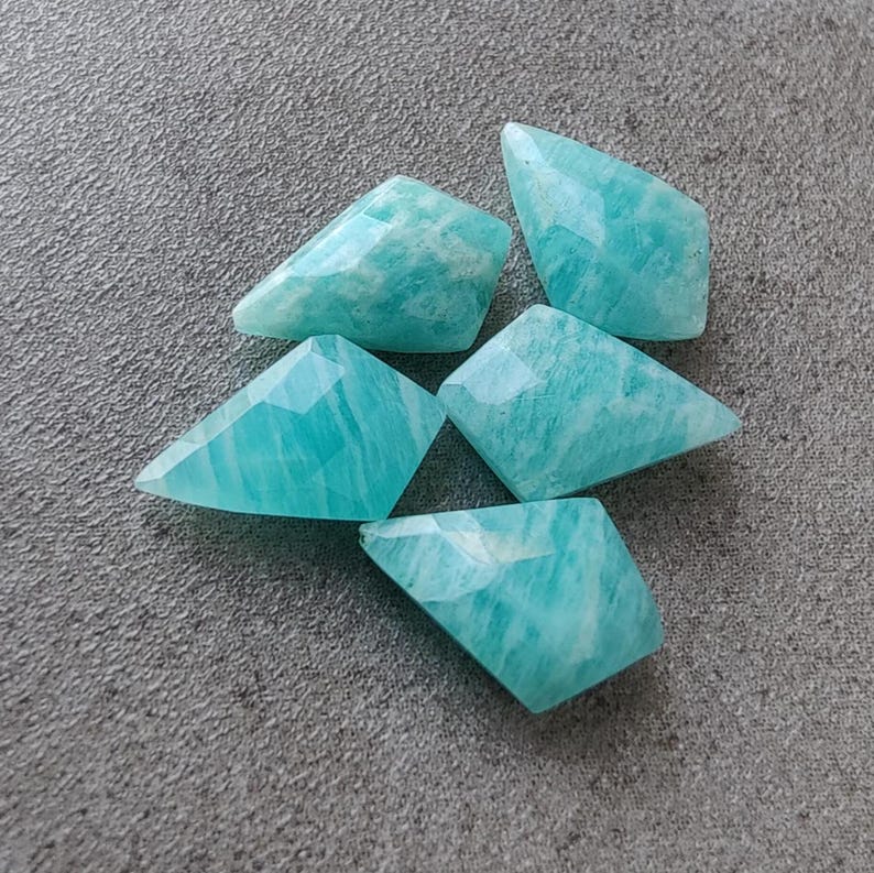 May include: Five teal green amazonite gemstone cabochons cut into a kite shape. The stones are faceted and have a translucent appearance.