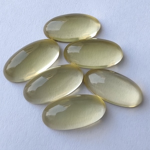 May include: Six oval-shaped, translucent yellow gemstones. The gemstones are smooth and have a slight sheen.