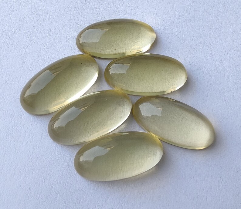 May include: Six oval-shaped, translucent yellow gemstones. The gemstones are smooth and have a slight sheen.
