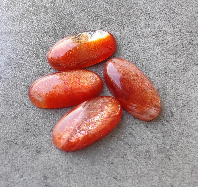 K&ouml;nnte beinhalten: Vier ovale Cabochons aus Sunstone in Orange- und Rott&ouml;nen mit schimmerndem, irisierendem Finish.