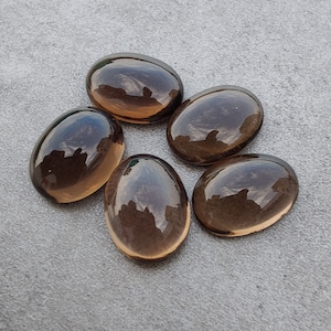 Puede incluir: Cinco piedras de cuarzo ahumado de forma ovalada, cada una con una superficie lisa y pulida. Las piedras son de color marrón oscuro y tienen una apariencia translúcida.
