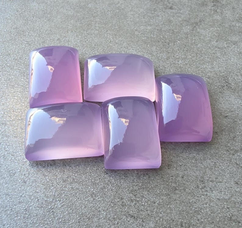 Pu&ograve; includere: Cinque pietre preziose rettangolari lavanda lucide con angoli arrotondati sono disposte su una superficie grigia. Le pietre hanno una qualit&agrave; traslucida, riflettendo la luce e creando riflessi. Le pietre preziose sono probabilmente per la creazione di gioielli o la collezione.