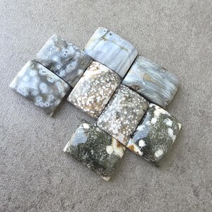 Könnte beinhalten: Eine Sammlung von neun rechteckigen Edelsteinen mit abgerundeten Kanten. Die Steine weisen eine Vielzahl von Mustern und Farben auf, darunter Weiß, Grau, Braun und Grün. Einige haben gesprenkelte oder marmorierte Designs, andere gestreifte.