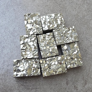 Peut inclure: Collection de pierres de pyrite rectangulaires à surface métallique et réfléchissante. Les pierres sont un mélange d'argent et d'or, avec un aspect mosaïque. Les pierres de pyrite sont disposées sur une surface grise.