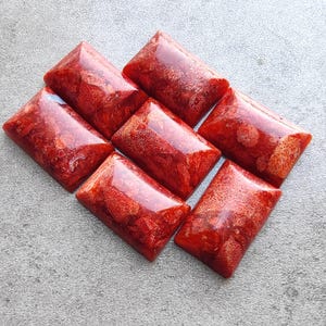 Pode incluir: Seis cabochões de coral vermelho, cada um com um padrão único de veios brancos, estão dispostos em um padrão escalonado sobre uma superfície cinza.