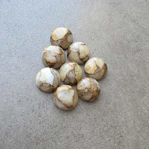 May include: Eight round, polished stones with a mix of white, tan, and gold colors. The stones have a marbled appearance with gold veining throughout. They are arranged in a loose cluster on a gray surface.