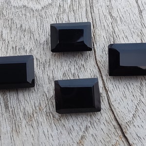 Pu&ograve; includere: Quattro pietre preziose rettangolari nere con taglio sfaccettato. Le pietre preziose sono disposte su una superficie di legno marrone chiaro.