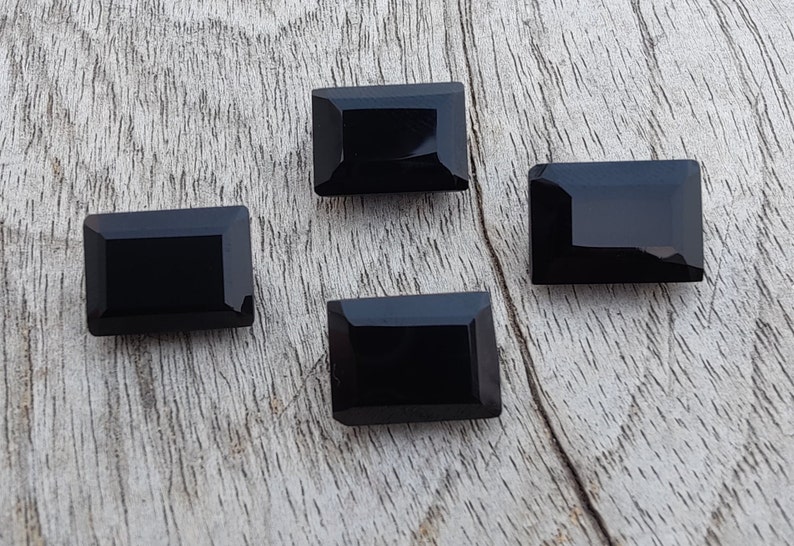 Pu&ograve; includere: Quattro pietre preziose rettangolari nere con taglio sfaccettato. Le pietre preziose sono disposte su una superficie di legno marrone chiaro.