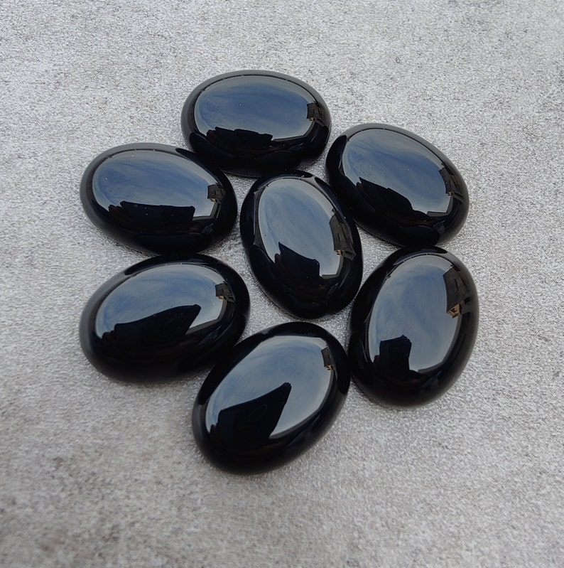 May include: Seven smooth, oval-shaped black gemstones. The stones are polished and have a glossy finish.