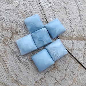 Op de afbeelding: Vijf vierkante, lichtblauwe cabochons met een marmerpatroon. De cabochons zijn in een cluster op een houten oppervlak gerangschikt.