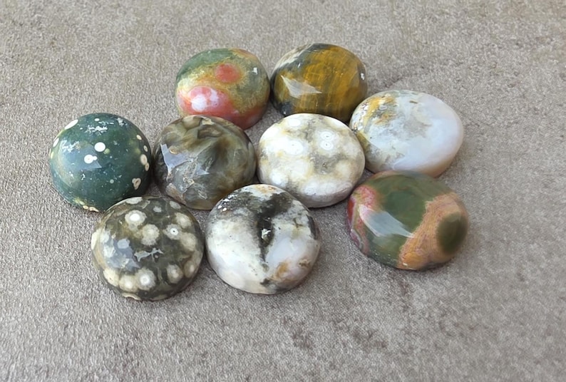 May include: A collection of nine polished stones in various colors, including green, brown, white, and red. The stones have a smooth, rounded shape and are likely used for decorative or metaphysical purposes.