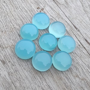 Pu&ograve; includere: Otto pietre preziose rotonde, lisce e di colore blu chiaro a cabochon. Le pietre sono disposte in cerchio su una superficie di legno chiaro.