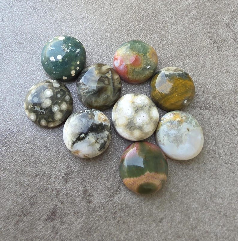 May include: A collection of nine polished gemstones in various colors, including green, brown, white, and yellow. The stones are round and have unique patterns and textures, suitable for jewelry making or collecting.