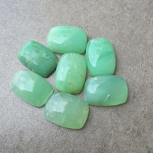 Può includere: Una collezione di sette pietre preziose cabochon verde chiaro, levigate e lisce, con una forma rettangolare arrotondata. Ogni pietra mostra una qualità traslucida con sottili variazioni nell'intensità del colore e nella trama interna.