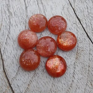 May include: Seven round, smooth, orange-red sunstone cabochons with a glittery, iridescent finish.