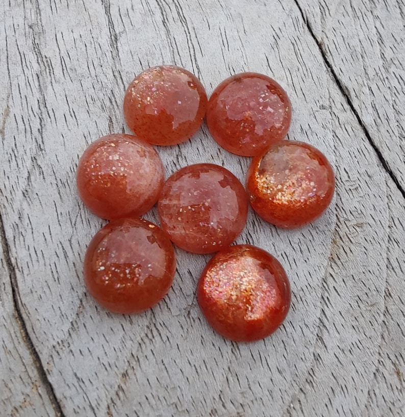 May include: Seven round, smooth, orange-red sunstone cabochons with a glittery, iridescent finish.