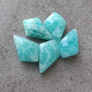 May include: Five teal green, faceted, gemstone beads. The beads are shaped like a diamond with rounded edges.