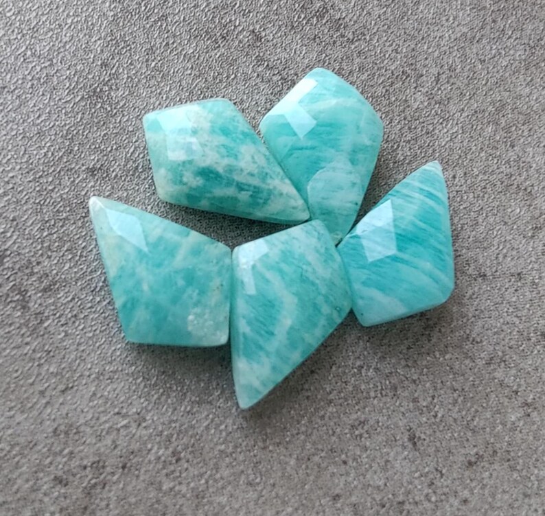 May include: Five teal green, faceted, gemstone beads. The beads are shaped like a diamond with rounded edges.