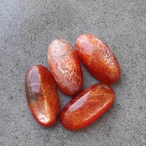 K&ouml;nnte beinhalten: Vier ovale Cabochons aus Sunstone in Orange- und Rott&ouml;nen mit schimmerndem, irisierendem Finish.